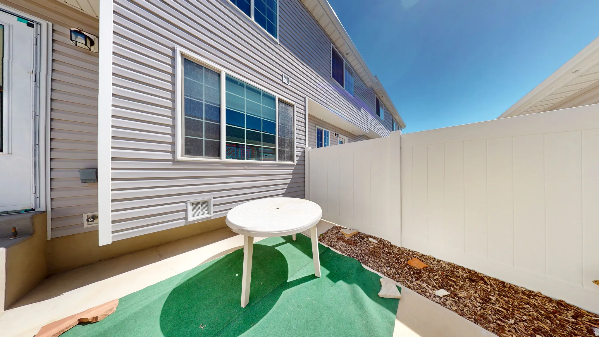 Private outdoor patio space featuring light gray siding and a white privacy fence