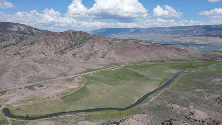 Expansive land parcel featuring a winding river, verdant fields, and rugged mountain terrain