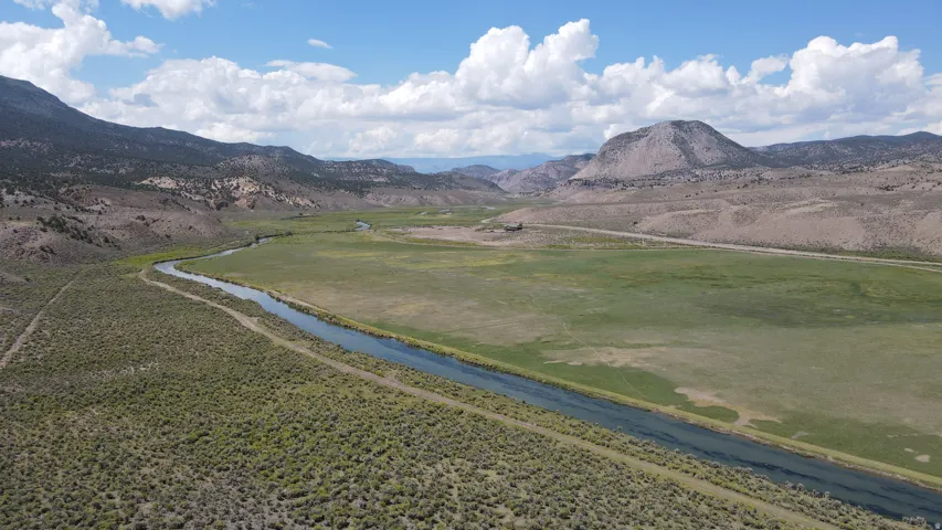 Expansive natural landscape featuring a winding river, a broad green plain, and distant mountains