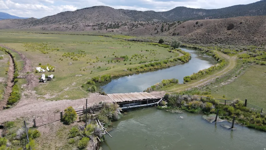 Expansive natural landscape featuring a winding river, a rustic wooden bridge, and rolling hills