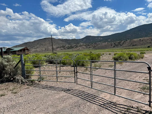 Metal gate on a gravel drive with a log-style home in the background