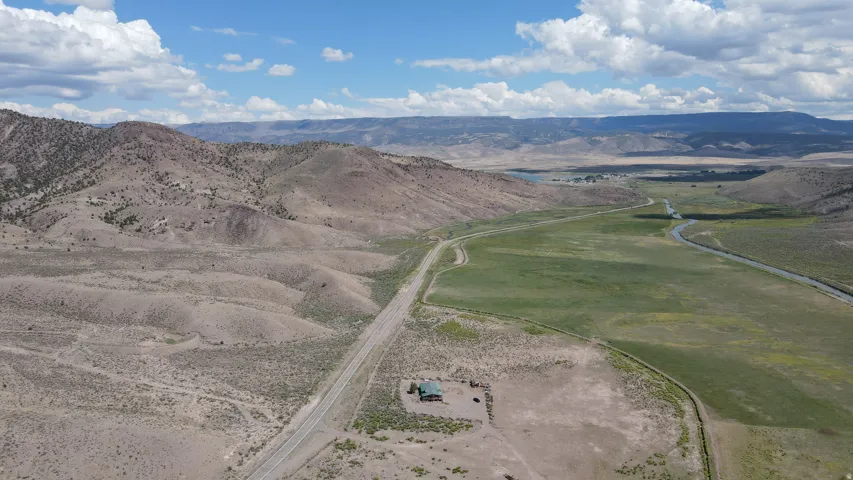 Expansive desert landscape featuring a single-story dwelling with a green roof, positioned alongside a paved road