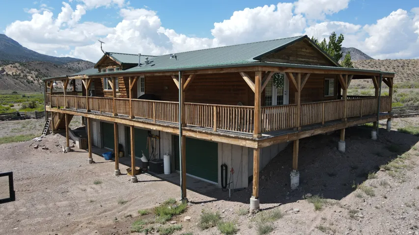 Log cabin exterior featuring a green metal roof, a full-length covered porch with wood railings and supports, and a lower-level with green access doors