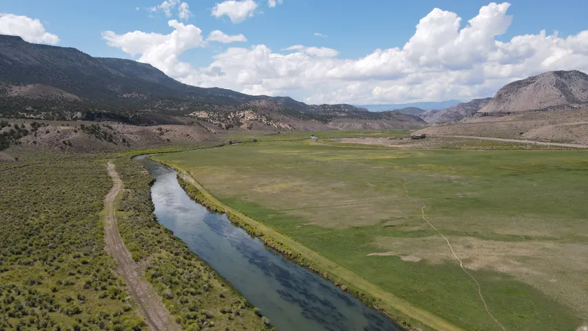 Expansive natural landscape featuring a river, verdant fields, and distant mountainous terrain