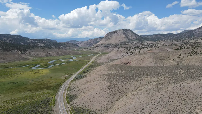 Expansive mountain valley landscape featuring a winding river, a paved highway, and diverse natural terrain