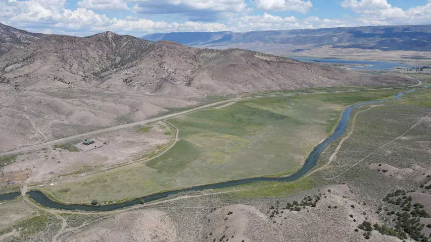 Expansive land parcel featuring a winding river, green fields, surrounding hills, distant lake, and a single structure