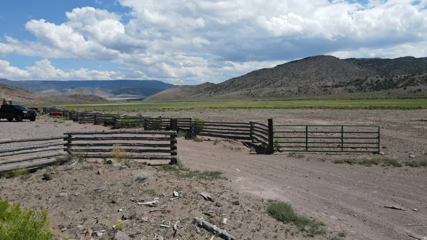 Extensive rural property featuring a large dirt track, rustic log fencing, and a metal gate