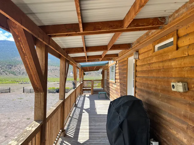 Expansive covered porch featuring wood flooring, wood railings, and exposed wooden beams supporting a metal roof