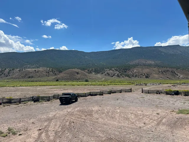 Expansive open land featuring rustic split-rail fencing, a gravel drive, and distant mountain scenery