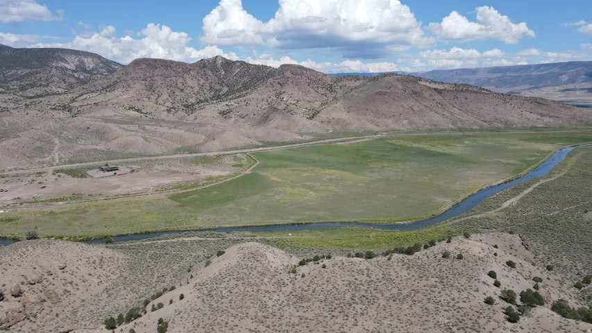 Expansive landscape featuring mountainous terrain, a winding river, and verdant fields