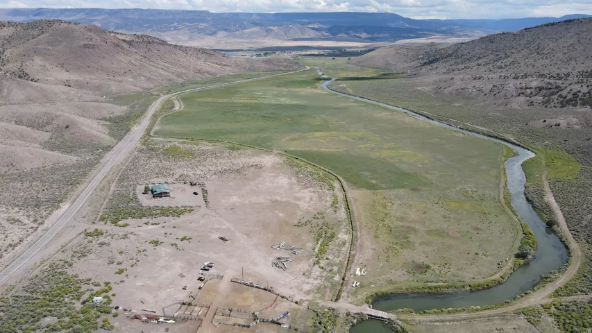 Expansive valley property featuring a winding river, a substantial green pasture, and a paved roadway