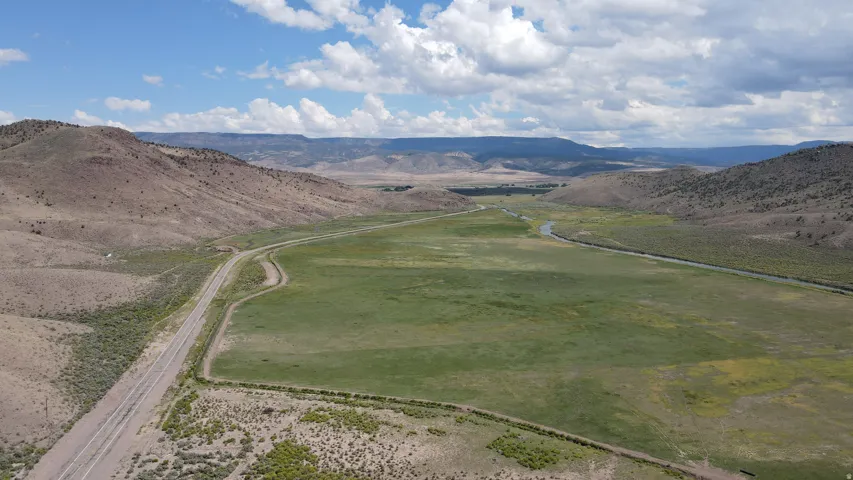 Expansive green fields bordered by natural terrain, featuring a winding river and distant mountains