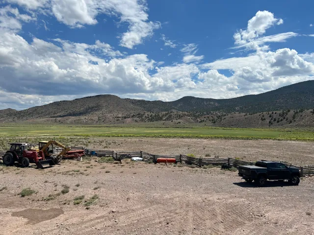 Expansive outdoor area featuring a split rail fence and a large, open field extending to distant hills