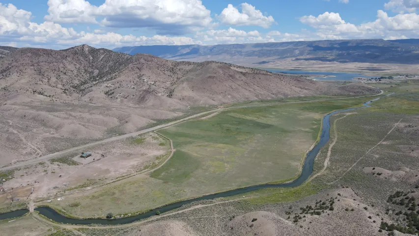 Expansive aerial of a natural landscape featuring a winding river, a large green field, and distant mountains
