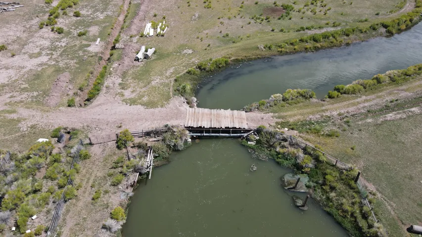 Wooden bridge spanning a waterway, surrounded by natural terrain and a secondary water channel