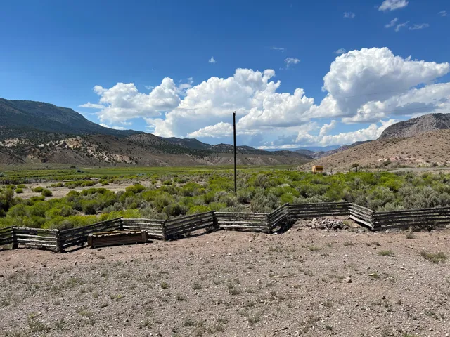 Expansive land parcel featuring a split-rail fence, diverse natural ground cover, and distant mountains