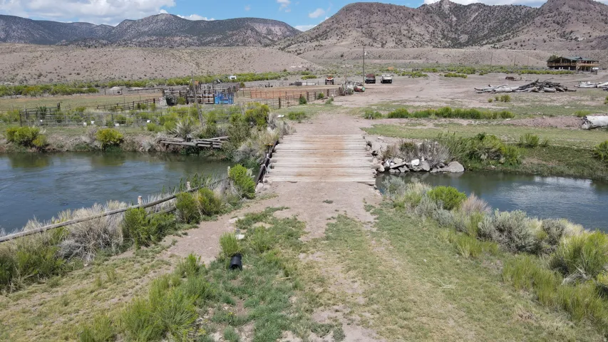 Wooden bridge crossing a flowing river, bordered by natural vegetation and distant mountains