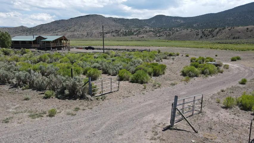 Gravel driveway leading to a raised structure with a wrap-around porch and a metal roof