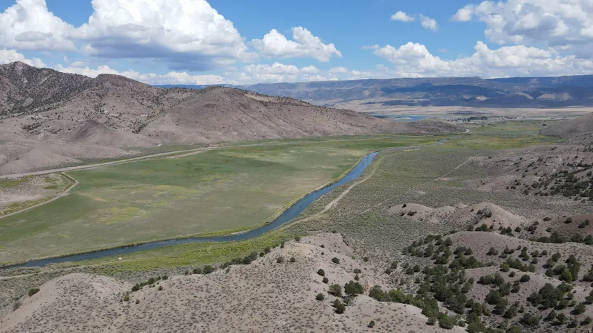 Expansive valley landscape featuring a river, verdant fields, and surrounding hillsides