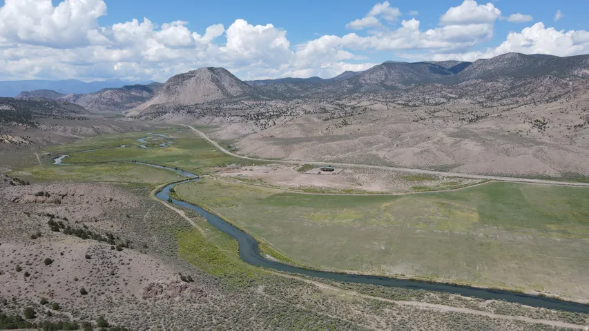 Expansive rural landscape featuring a winding river, verdant fields, rolling hills, and distant mountains