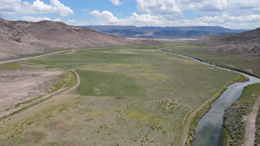 Expansive valley landscape featuring a winding river, verdant fields, and distant mountain ranges