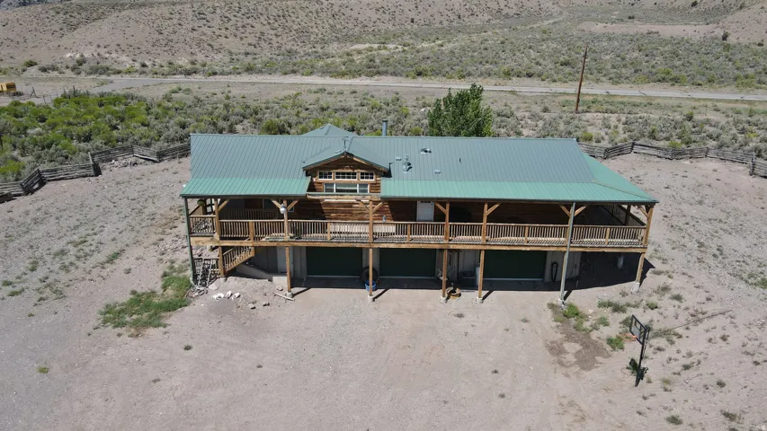 Raised log cabin style residence featuring a green metal roof, a full-length covered deck with wooden railings, and multiple ground-level garage bays