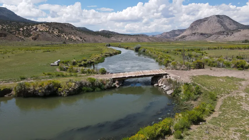 Expansive natural landscape featuring a flowing river, a rustic wooden bridge, and verdant riparian areas
