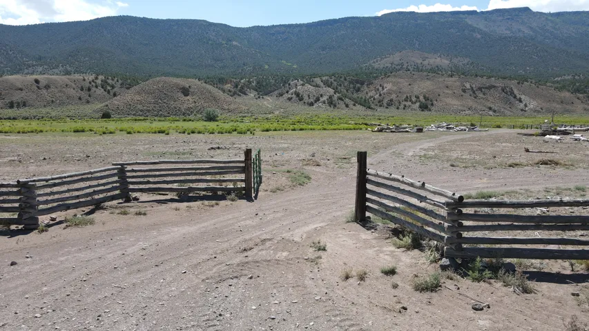 Rustic log fencing framing a dirt road entrance, with expansive open land and distant mountains