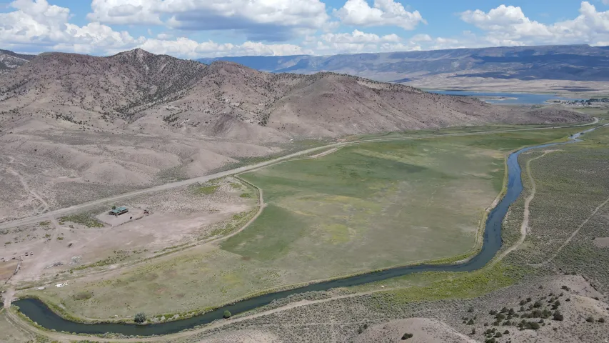 Expansive natural landscape featuring a winding river, verdant fields, a single structure, and distant mountains