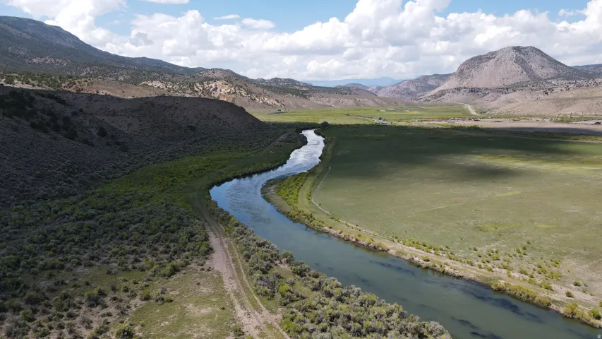 Winding river traversing expansive green fields and rugged, vegetation-covered hills
