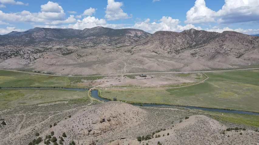 Expansive acreage featuring a winding river, mature green fields, and distant mountain ranges under a partly cloudy sky