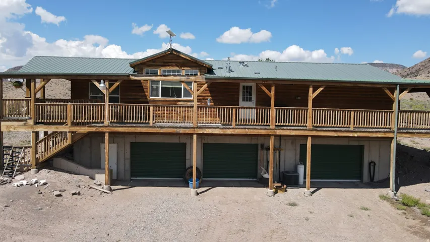 Log cabin style home featuring an expansive wrap-around deck with natural wood railings, a durable green metal roof, and three ground-level garage bays with green doors