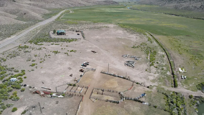 Expansive rural acreage featuring a two-story residence with a green roof, multiple fenced corrals, and a graded access road