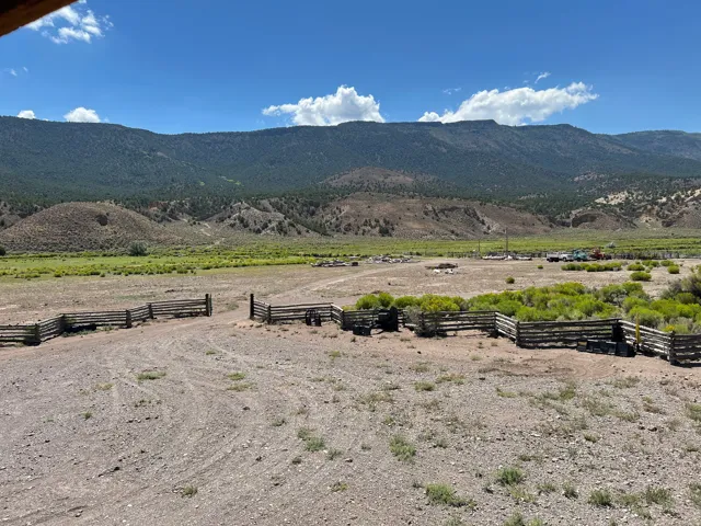 Expansive open land featuring rustic split-rail fencing, a gravel path, and distant mountainous terrain
