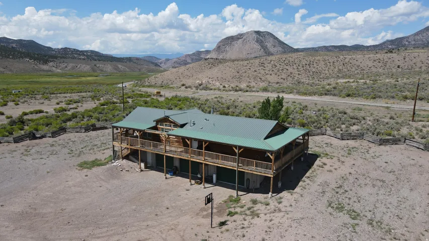Rustic two-story home featuring a green metal roof and a full-length upper deck with wood railings