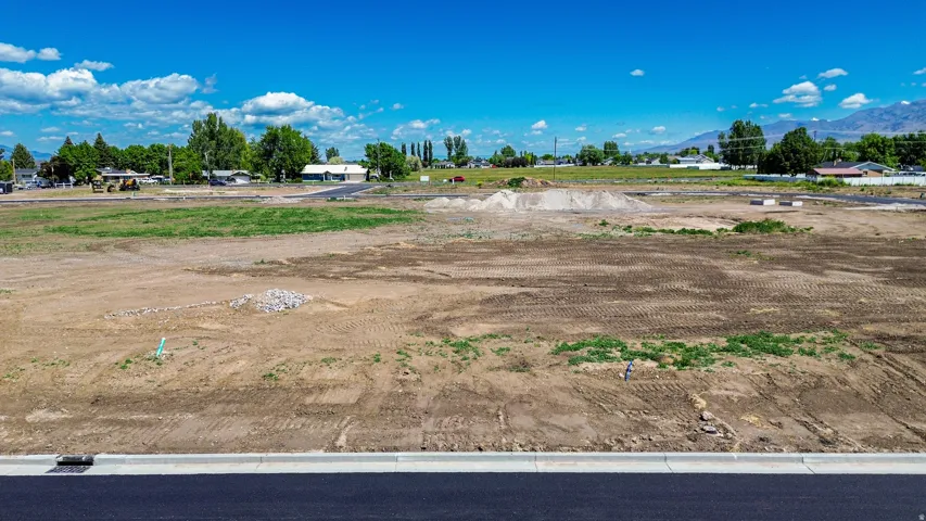 Expansive level lot featuring clear terrain, newly paved road frontage, and distant mountain scenery under a clear sky