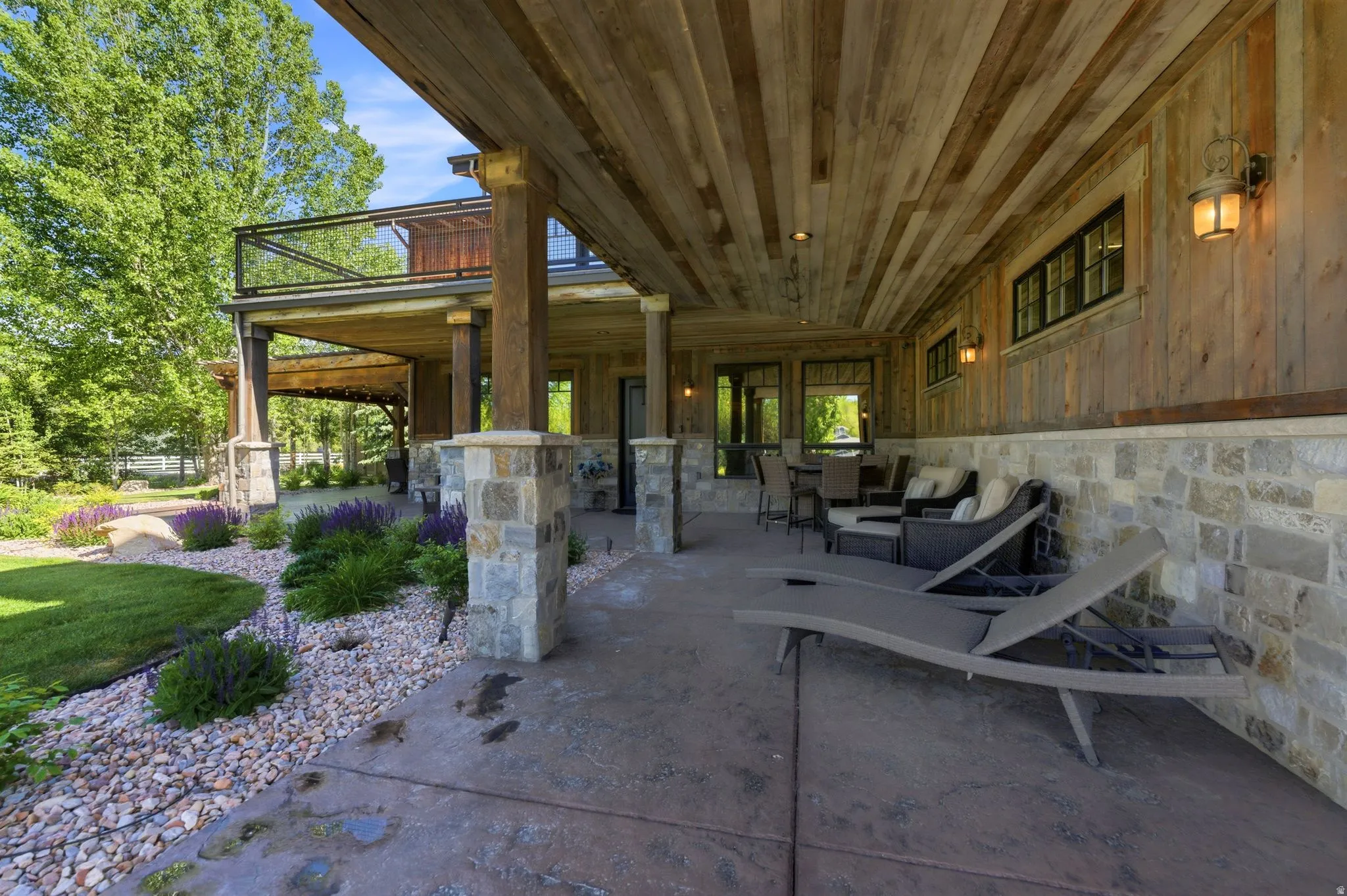 Expansive covered patio featuring a wood-finish ceiling, stone and wood-paneled walls, multiple wall sconces, and a concrete patio floor