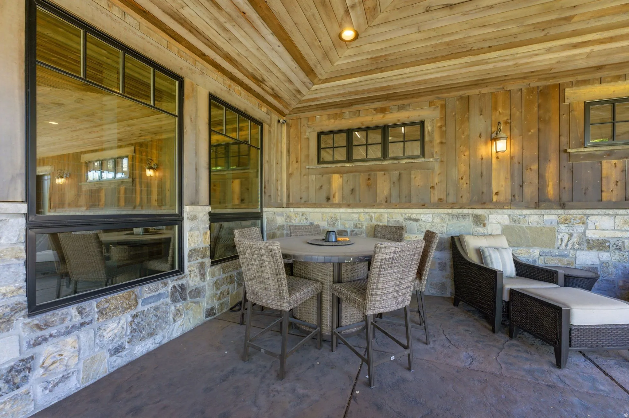 Covered patio featuring a wood plank ceiling, stone and wood panel walls, and stamped concrete flooring
