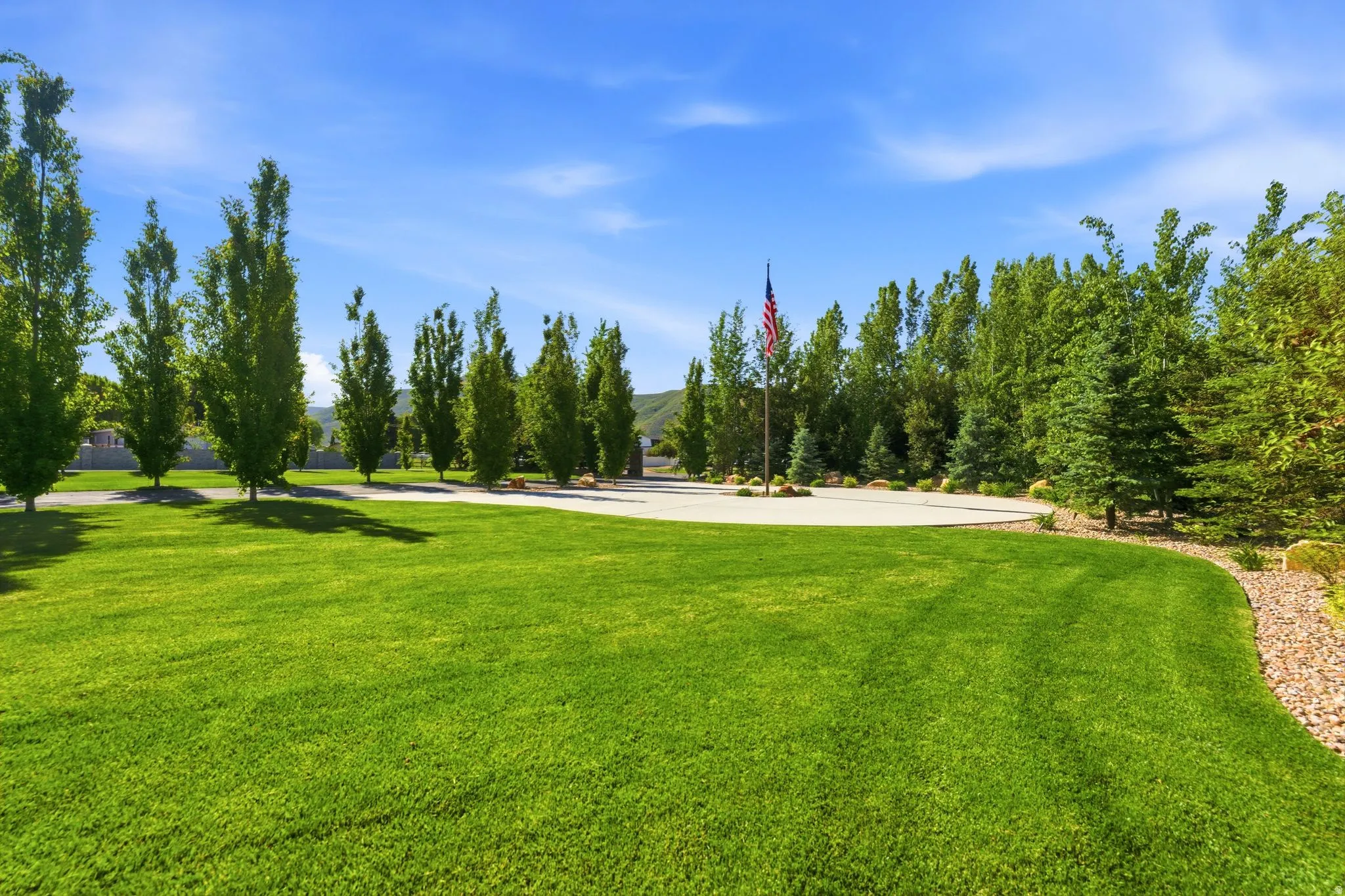 Expansive lawn with mature trees, a paved driveway, and a central flagpole
