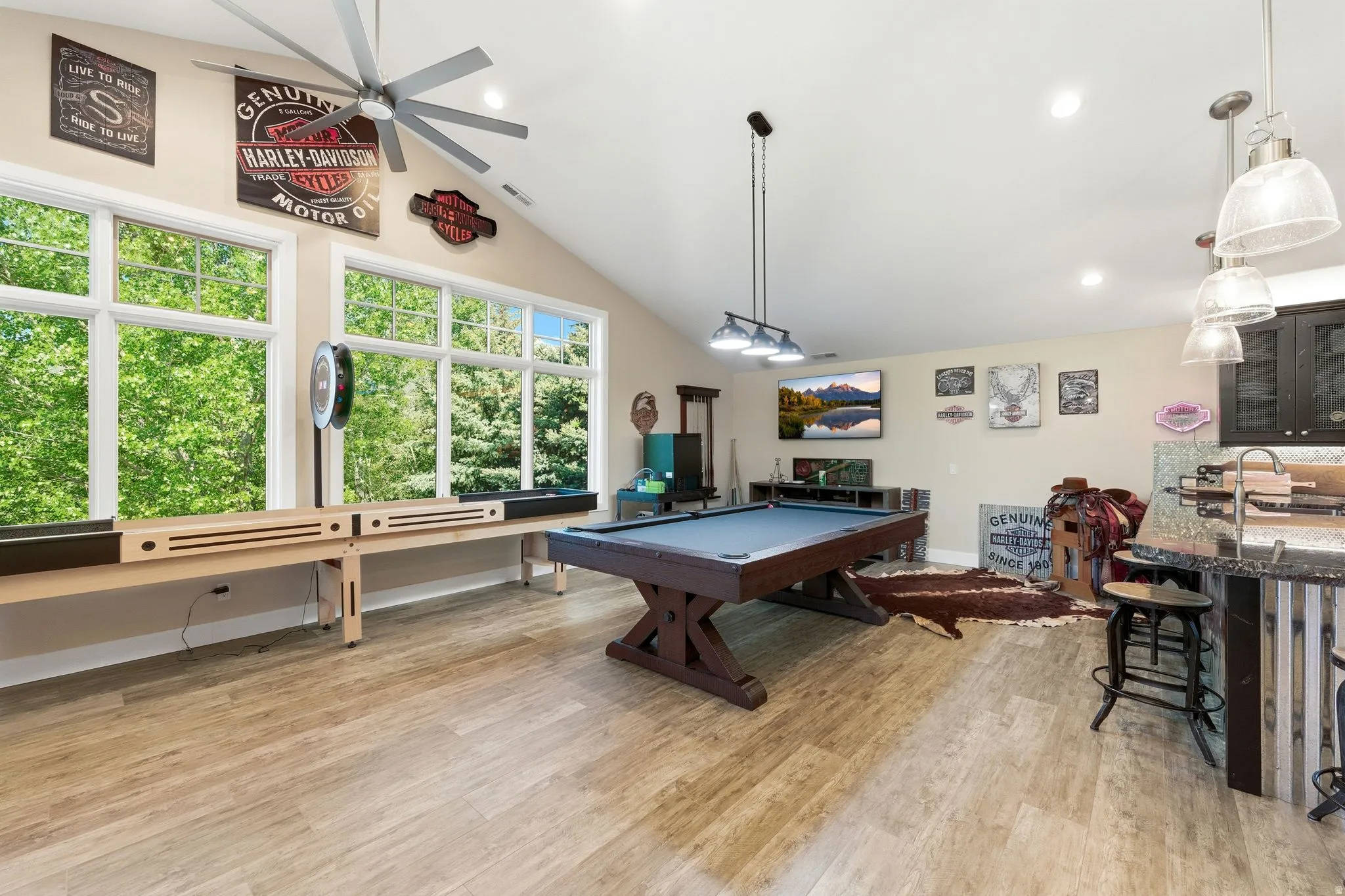 Spacious recreational area featuring vaulted ceilings, large windows, wood-finish flooring, a built-in wet bar with pendant lighting, and recessed lighting