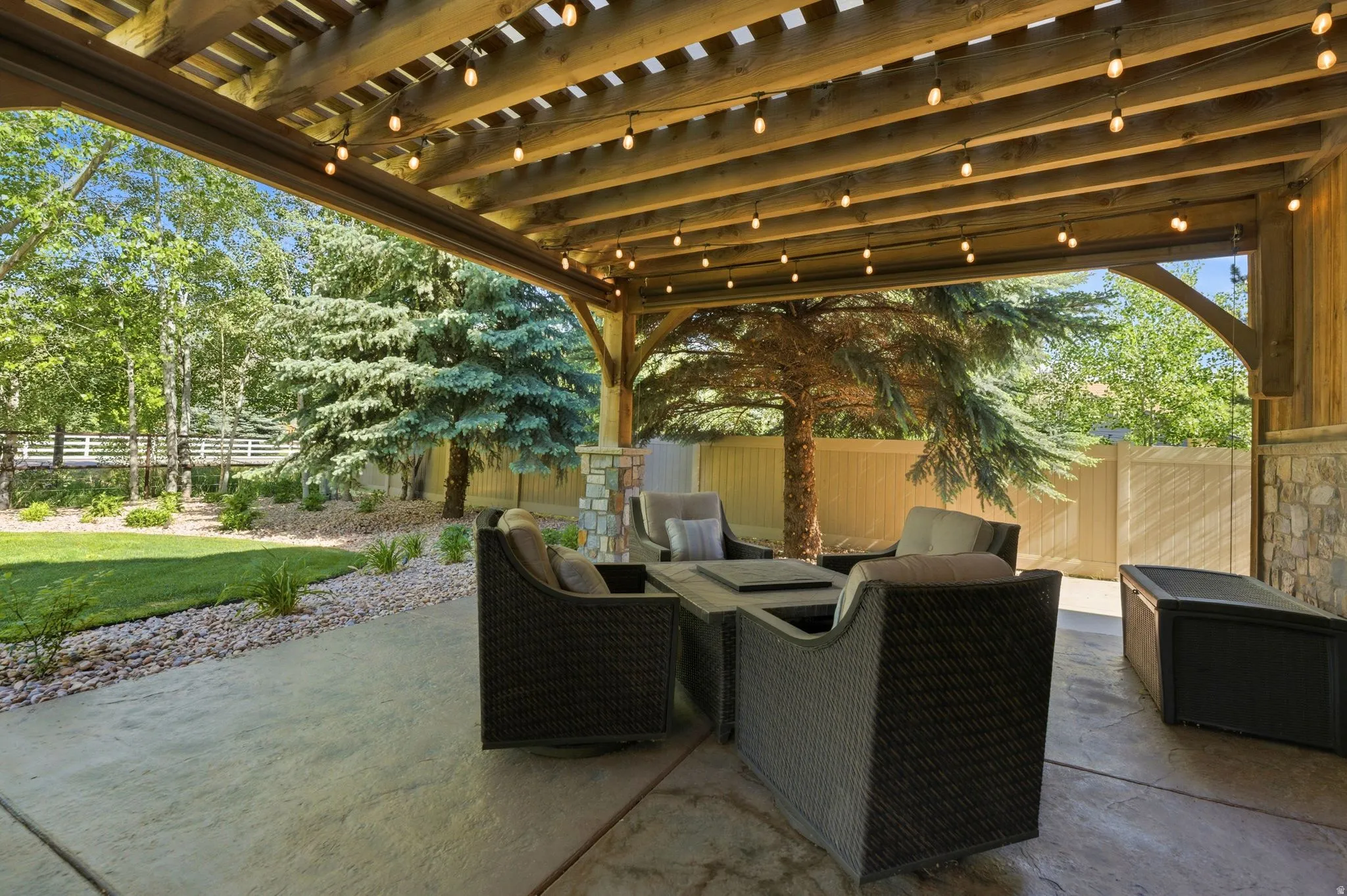 Expansive patio featuring a wood beam pergola with string lighting, concrete flooring, and a stone accent wall