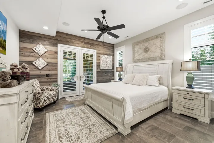 Room featuring a wood-panel accent wall, tile flooring, and white French doors with louvered shutters