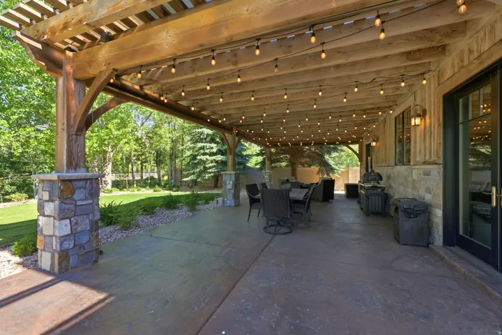 Expansive covered patio featuring a wood pergola, string lighting, and stone-clad columns