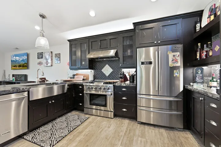 Gourmet kitchen featuring dark cabinetry, stainless steel appliances, granite countertops, a farmhouse sink, and wood-finish flooring