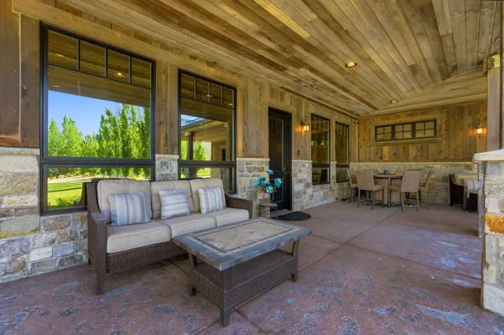 Spacious covered patio featuring a wood-panel ceiling, stone accents, large black-framed windows, and stamped concrete flooring