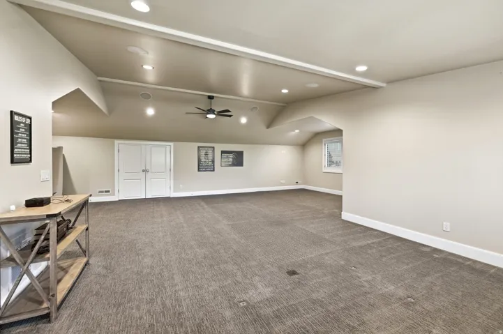 Spacious room featuring neutral carpeting, recessed lighting, double panel doors, and a ceiling fan