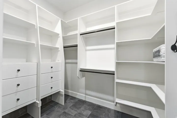 Custom-designed closet system featuring white shelving, multiple drawers with dark hardware, and integrated hanging rods
