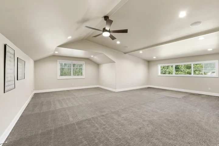 Spacious room featuring vaulted ceilings, recessed lighting, a modern ceiling fan, and multiple windows with white blinds