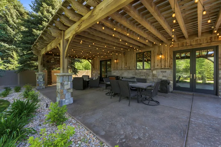 Expansive covered patio featuring a wood pergola, string lighting, and stone-wrapped structural columns