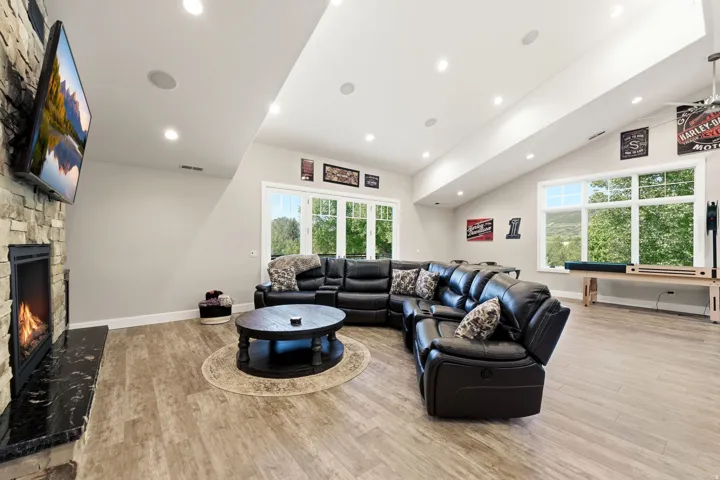 Spacious living area featuring wood-finish flooring, a stone-clad fireplace with a black stone hearth, recessed lighting, and large windows
